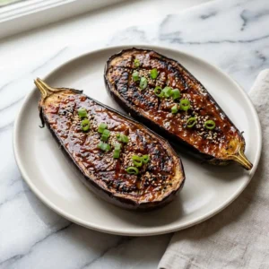 A hearty slice of baked eggplant parmesan with visible layers of eggplant, wilted spinach, and rich red tomato sauce. The top is blanketed in melted, bubbly mozzarella cheese, toasted to a golden brown and garnished with fresh basil leaves as a wisp of steam rises.